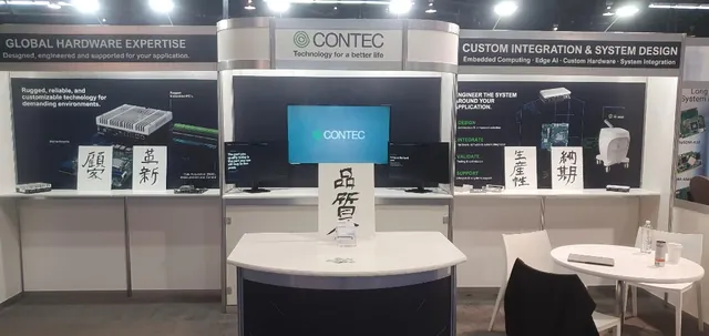 Contec&rsquo;s booth at Embedded World North America 2026 in Anaheim: a central promo screen flanked by the two kiosk monitors, under banners for hardware expertise and custom system design.