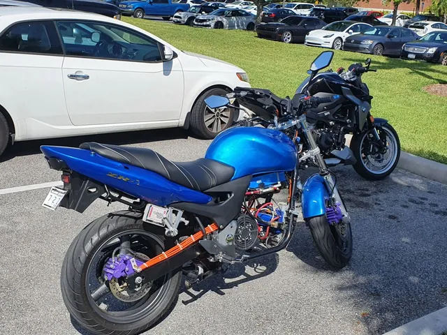 The motorcycle from the rear right: orange high-voltage cables along the swingarm, purple brake calipers and the cooling fan behind the battery.