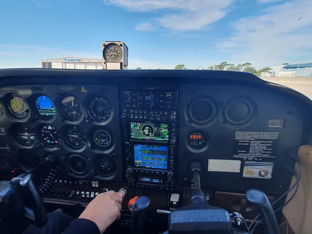 A light aircraft&rsquo;s instrument panel with Garmin avionics, seen from the left seat on a sunny ramp, tail number blurred.