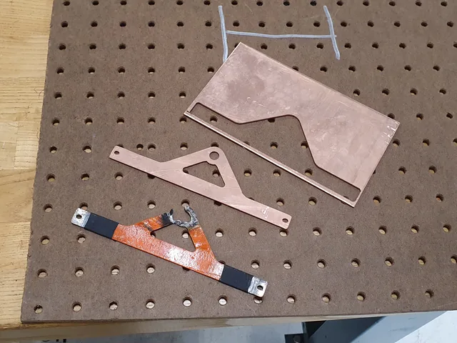 Copper on a pegboard: a flat waterjet-cut plate, a triangular busbar blank and a finished busbar with an orange coating and tinned ends.