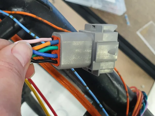 A hand holding a grey sealed multi-pin connector with colored wires seated in its seal.