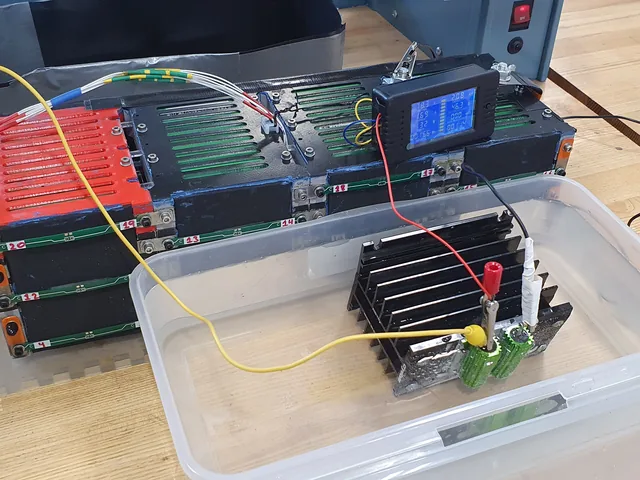 A battery pack wired to a finned load resistor in a plastic tub, with a panel meter and a red emergency-stop button.