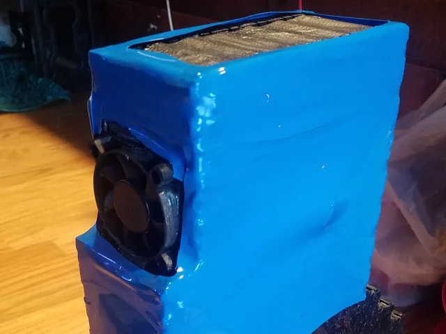 An early battery block coated in black with small cooling fans on its side and the top wrapped in blue heat-shrink.