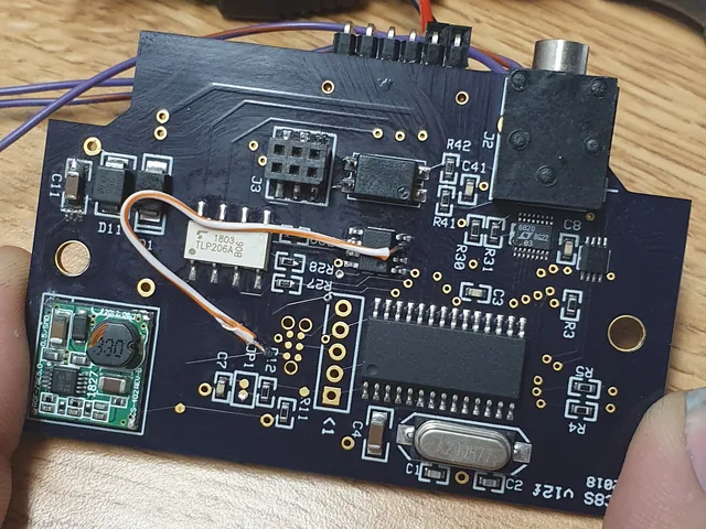 A custom dark-blue circuit board in hand, with a bodge wire added during rework.