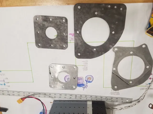Four cut steel and aluminum mounting plates laid on my hand-drawn wiring diagram, January 2020, with a battery module and a braided harness at the bottom.