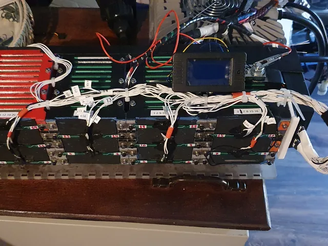 A battery pack with a bundle of white cell-sense wires, each tagged with a printed label and tied down along the top.