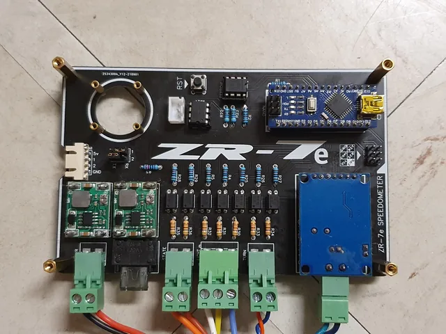The assembled black ZR-7e speedometer interface board with an Arduino Nano, two buck converters, a row of optocouplers and green screw terminals.